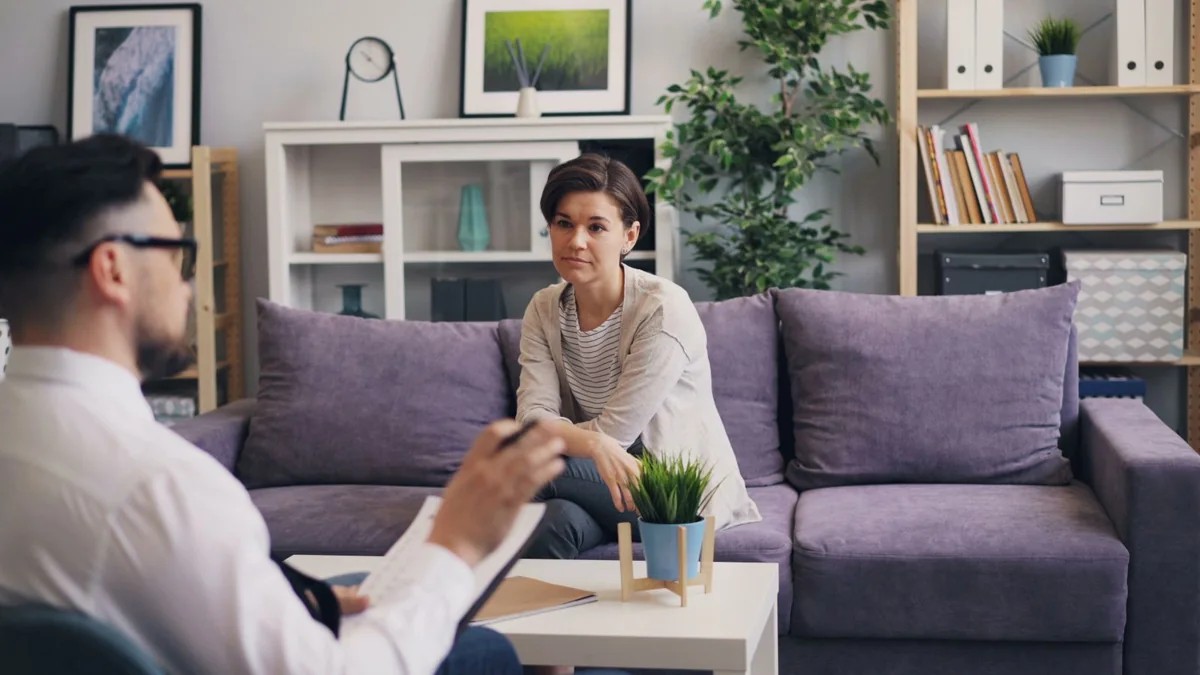 Two people having a professional conversation beside a purple sofa.